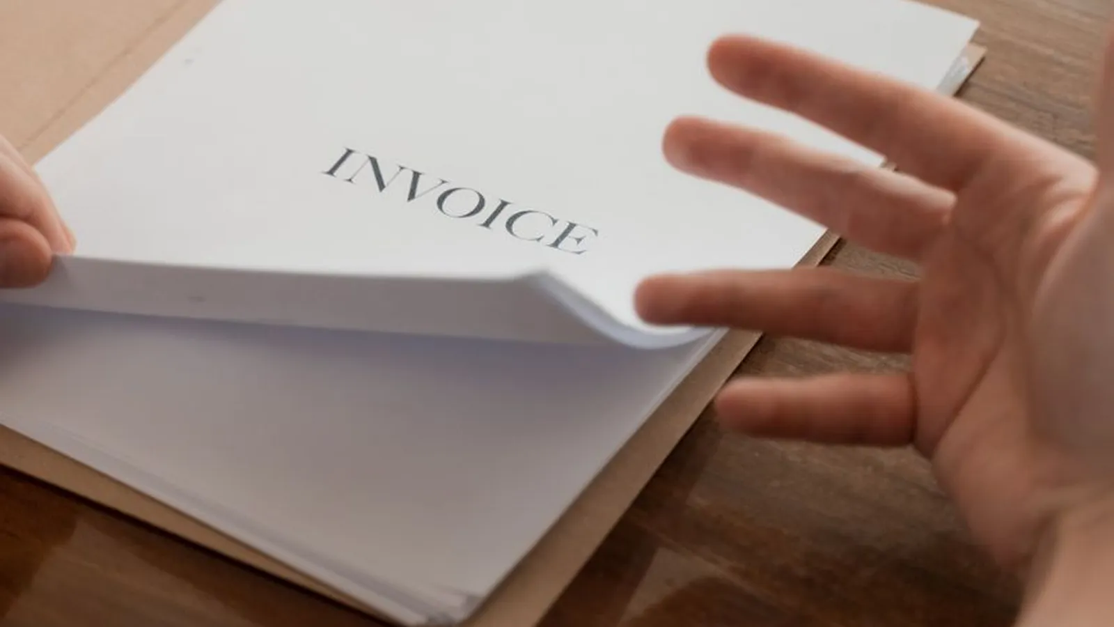 A hand holding an invoice document, representing the paperwork behind billing and invoice fraud