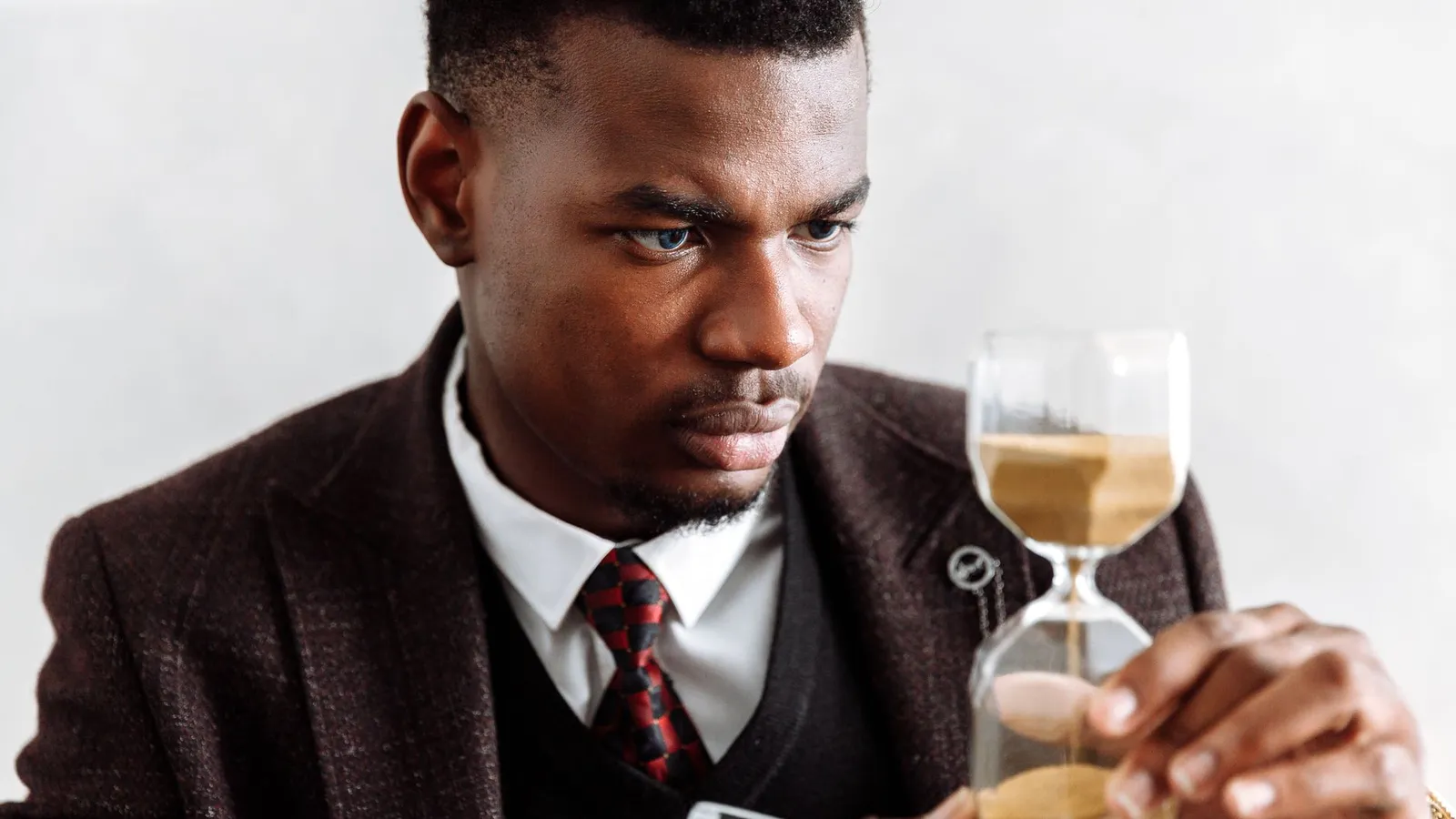 A man in a waistcoat holding an hourglass at his desk, representing the moment of deciding to act before picking up the phone to call an investigator