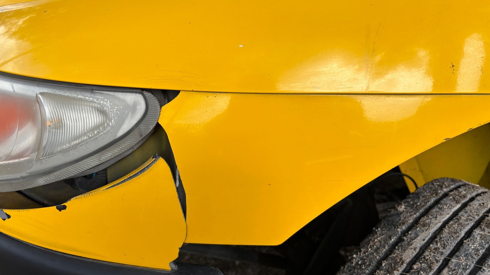 Close-up of vehicle damage to a headlight and front panel from a motor accident insurance claim