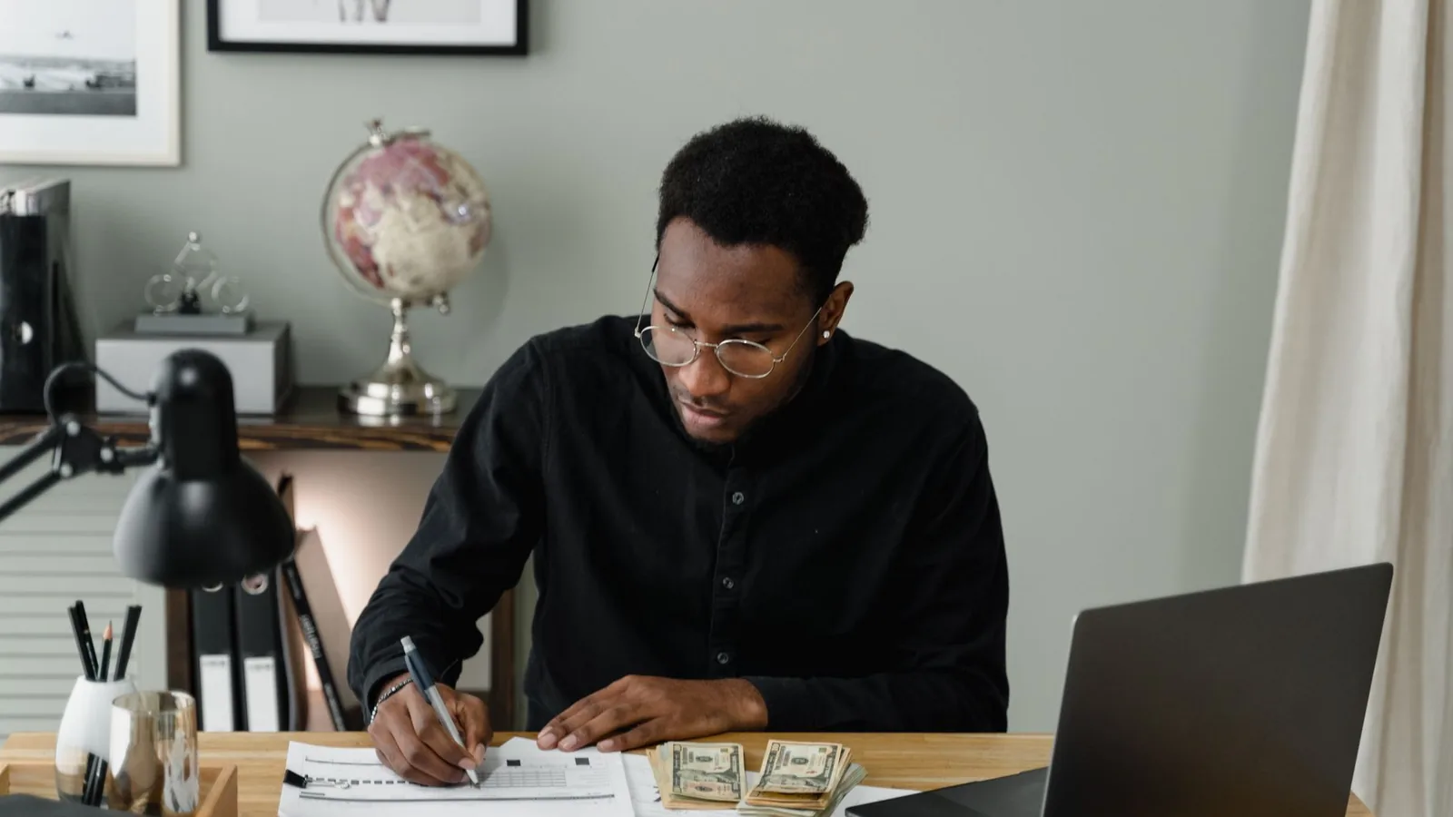 An African man reviewing financial documents and cash at a desk, representing monitoring fraud risk in a remote operation
