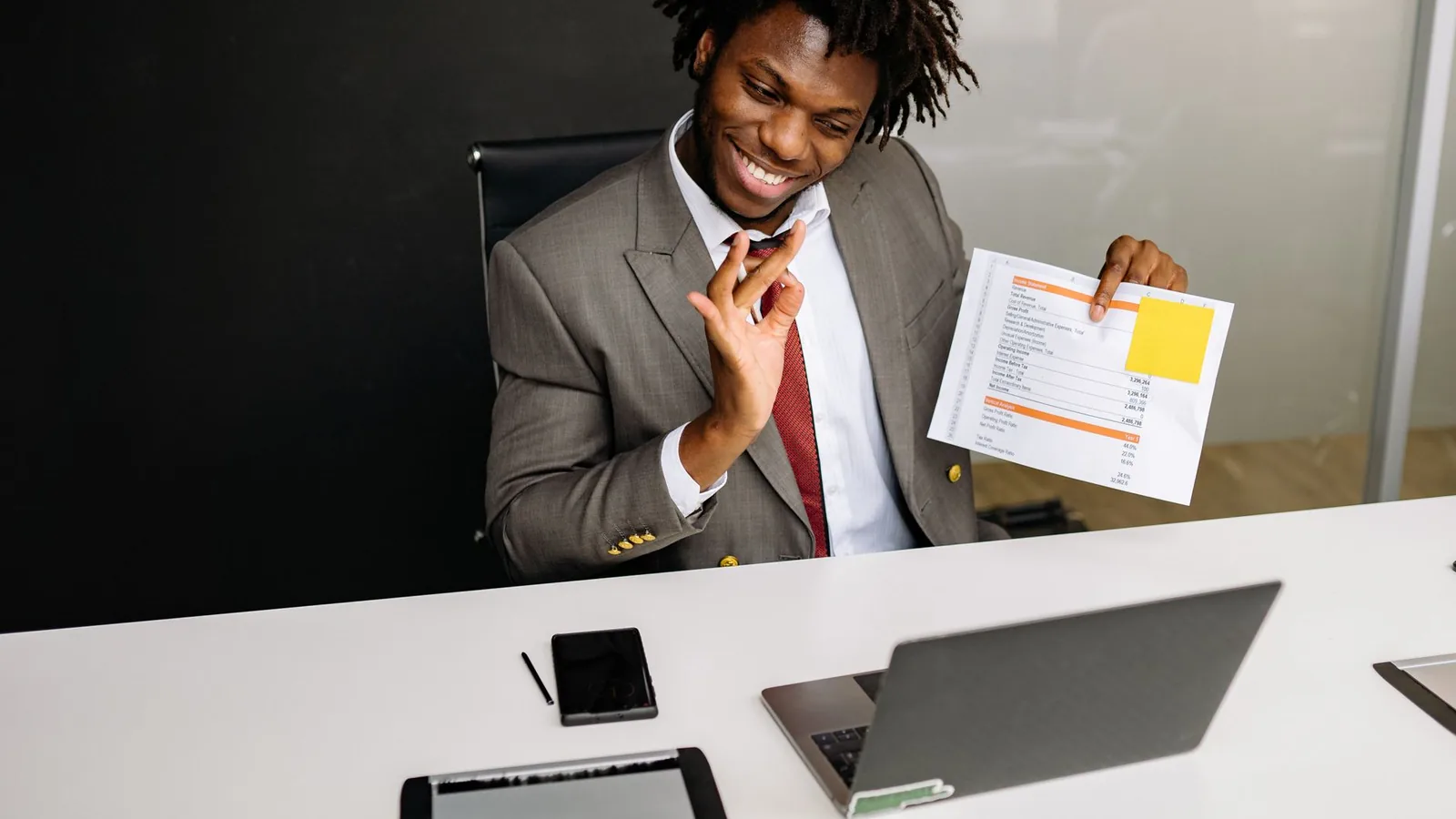A businessman smiling while holding up a sales report during a video call, representing verifying a local distributor's reported sales figures