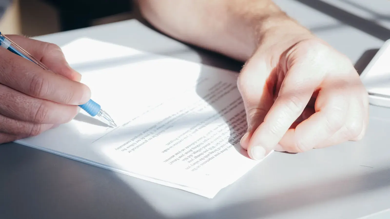 Two hands over a signed document with a pen, representing a second-signature approval control