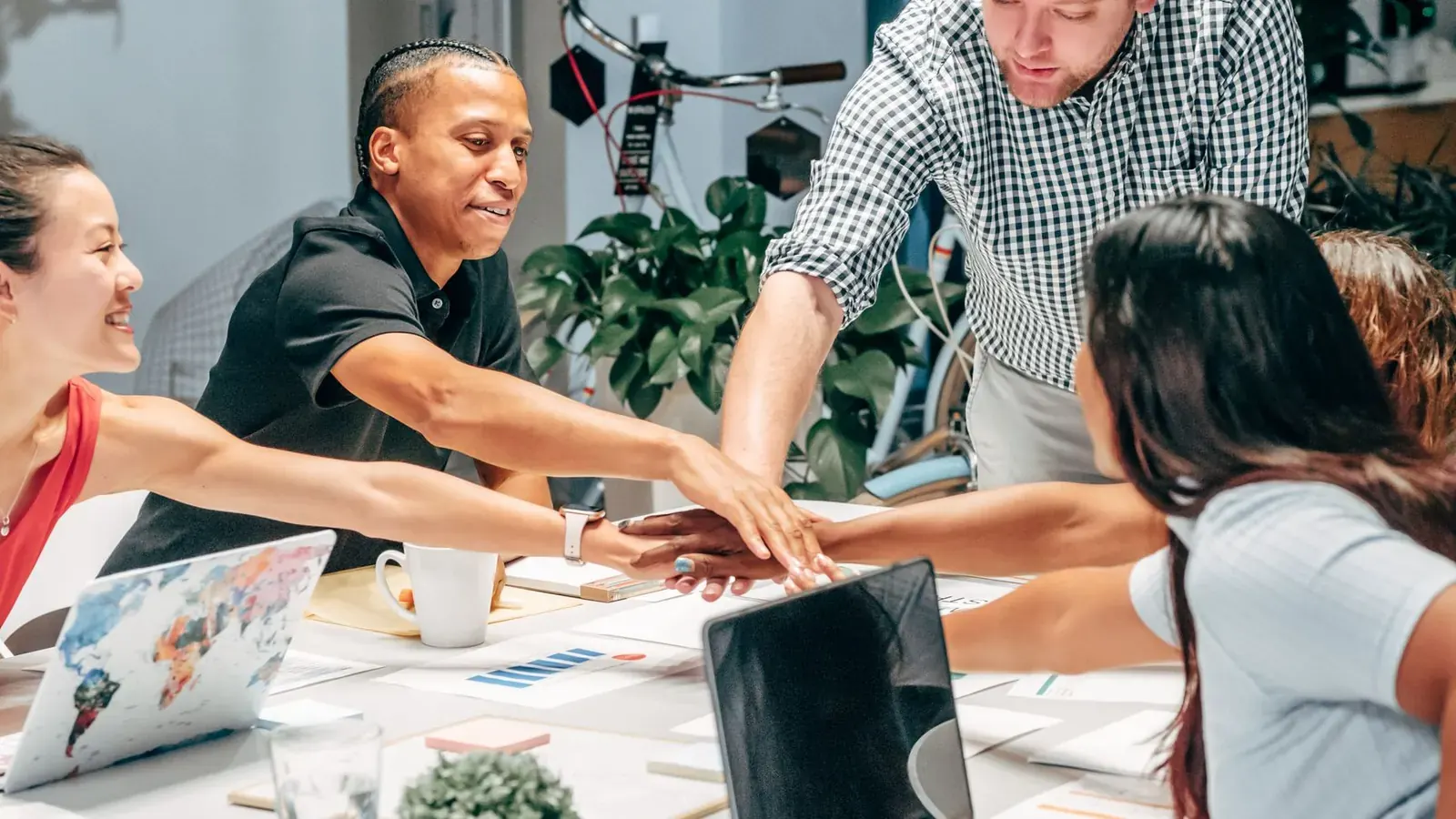 A diverse team joining hands together over a table in an office meeting, representing a culture where raising concerns feels safe