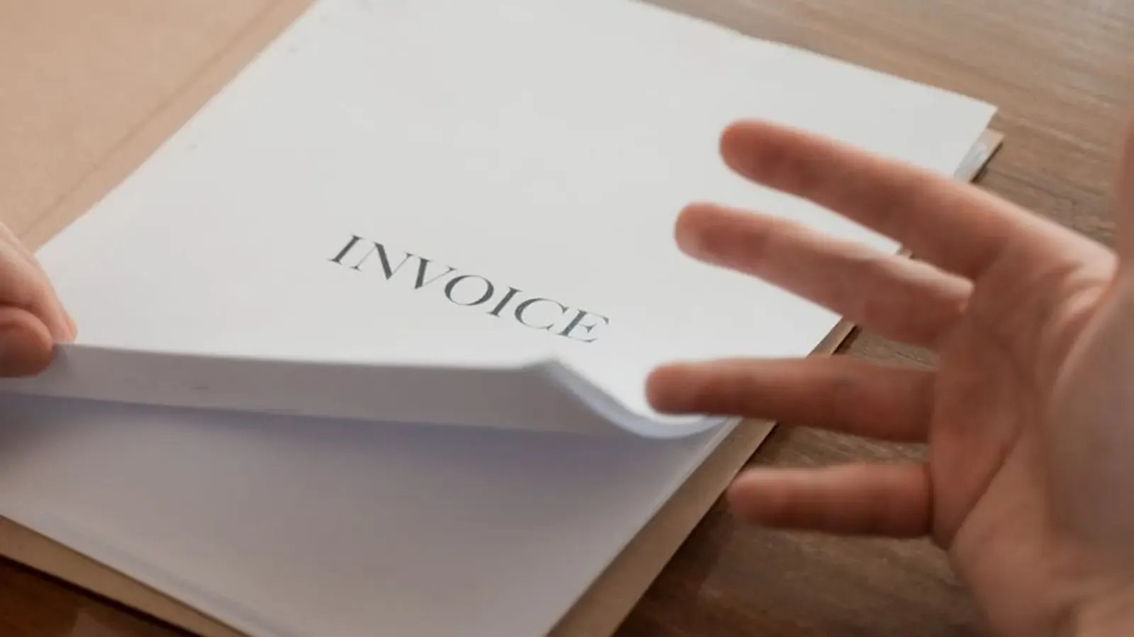 Close-up of a hand opening a folder labeled Invoice on an office desk, representing invoice and procurement fraud