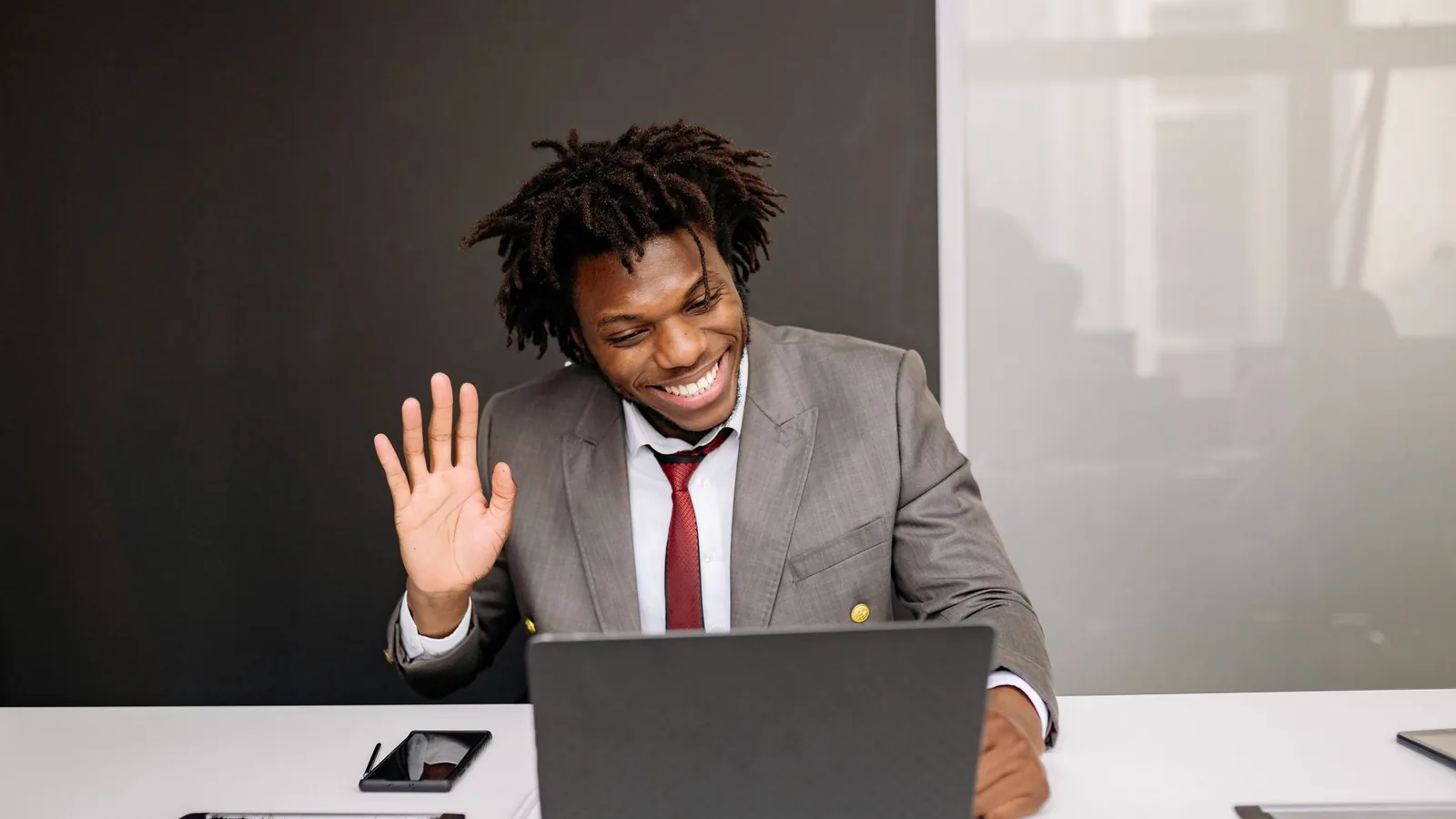 An African businessman smiling and waving during a video call on his laptop, representing an international business meeting