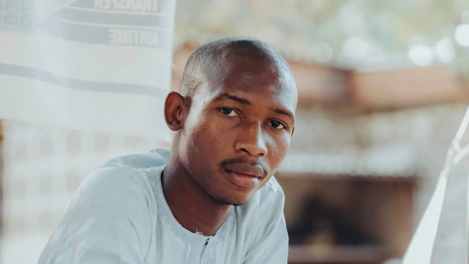 A local shopkeeper in Tanzania standing behind his counter, representing the kind of on-the-ground business verification only a local presence can provide