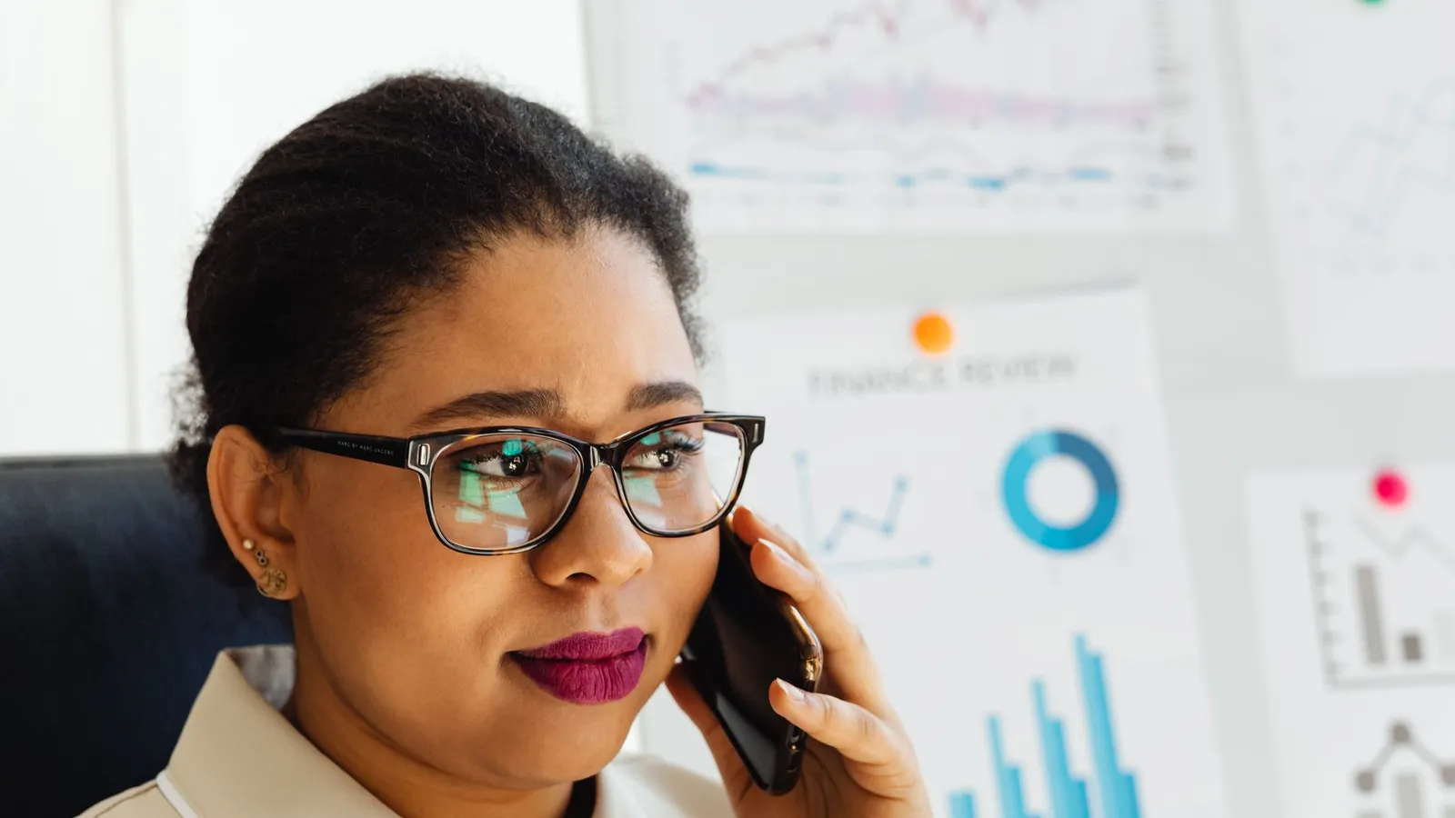 A businesswoman on the phone in front of a wall of financial charts, representing a policyholder raising a disputed valuation with evidence behind it