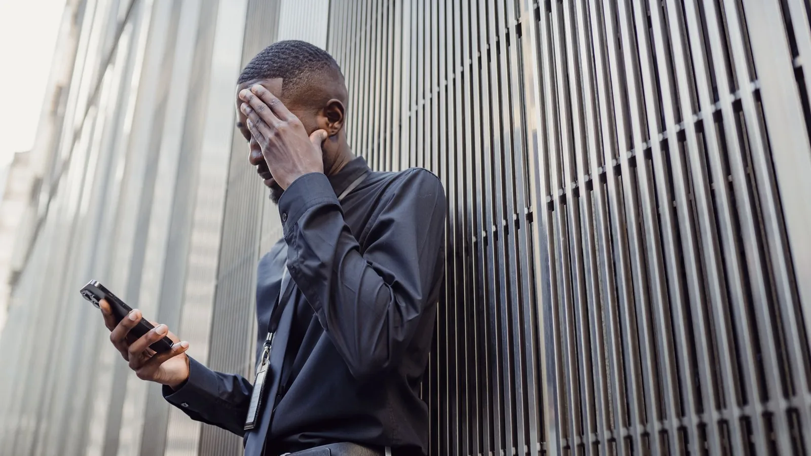 A man outside an office building looking troubled while checking his phone, representing the legal line an investigator should never cross when gathering evidence