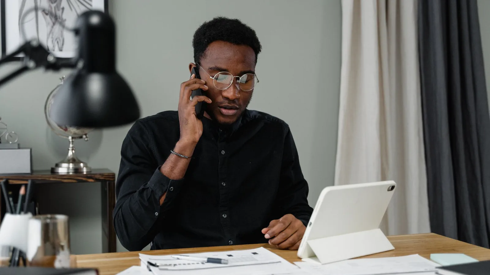 A man on the phone reviewing a tablet at his desk, representing a client verifying a firm's TIRA registration before hiring