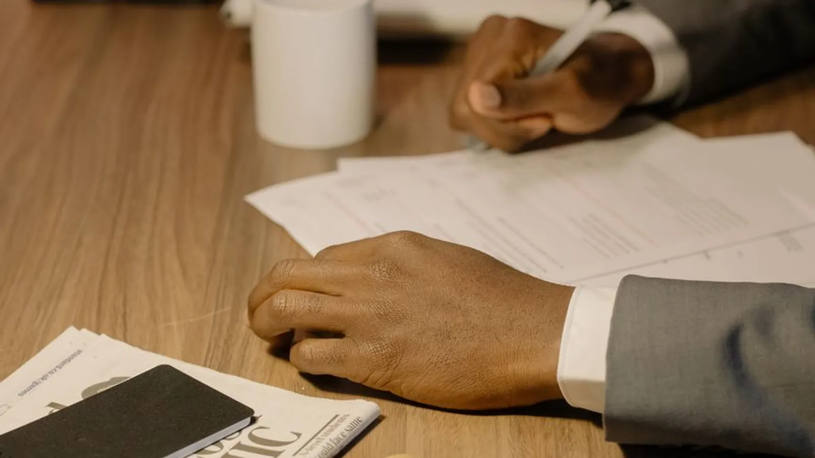 A hand writing notes beside a magnifying glass and case folders on a desk, representing the documented process behind evidence that holds up under scrutiny