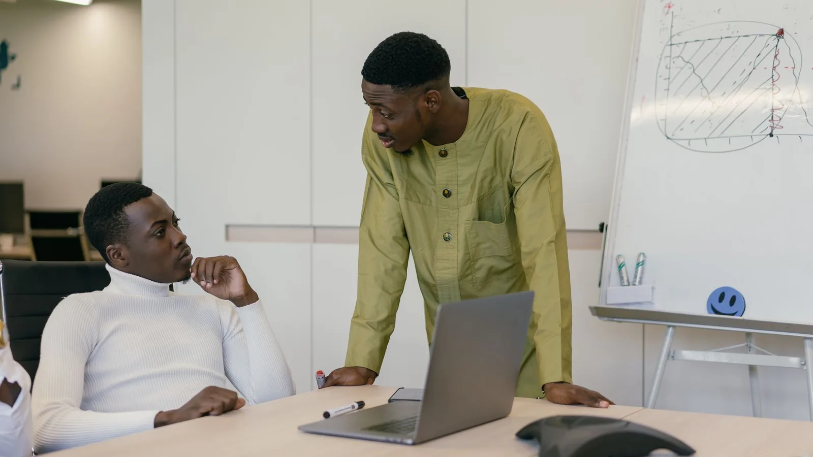 Two co-founders discussing a business plan around a laptop in a meeting room, representing verifying a co-founder before splitting equity