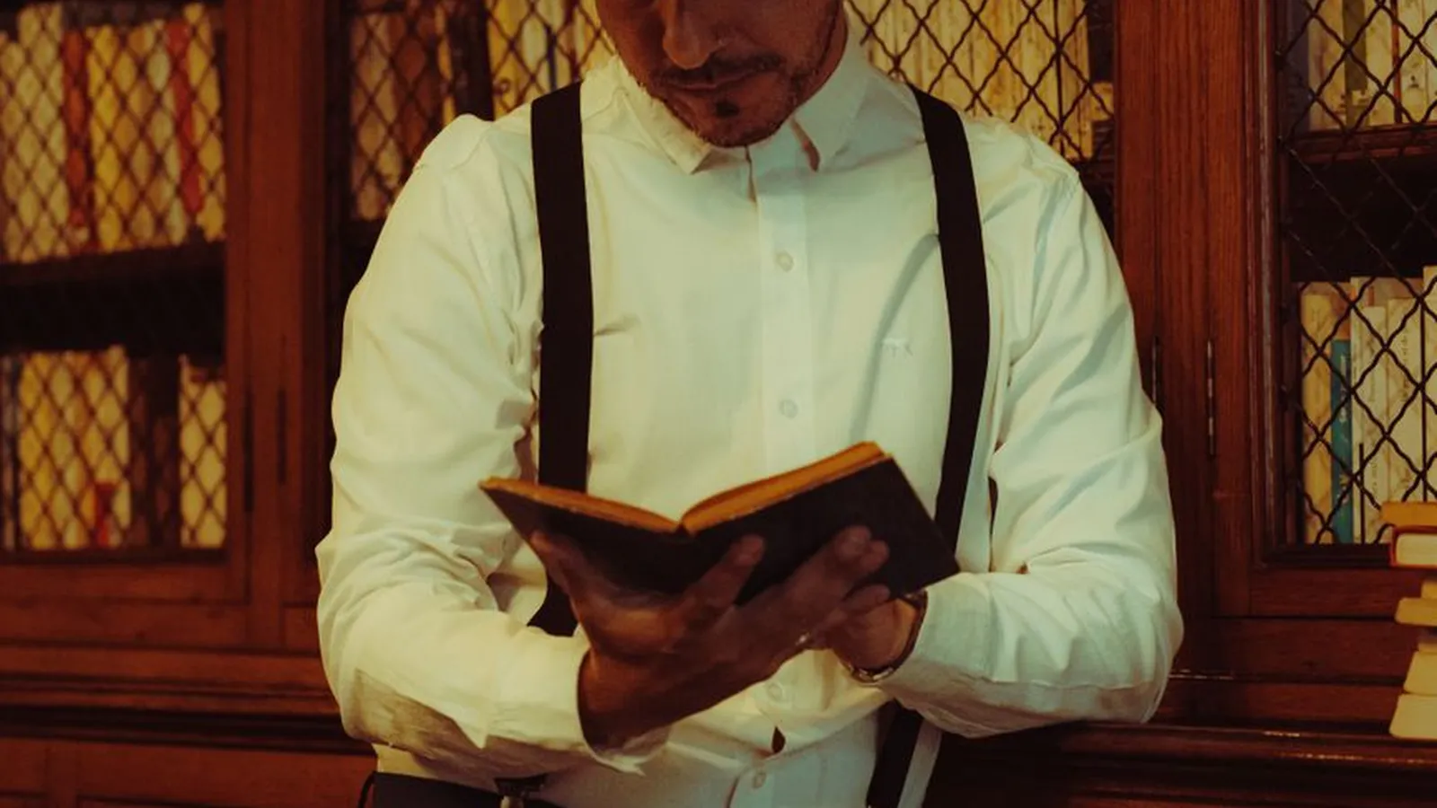 A man reading an old book in a wood-paneled library, representing the vintage, fictional image the word detective still carries
