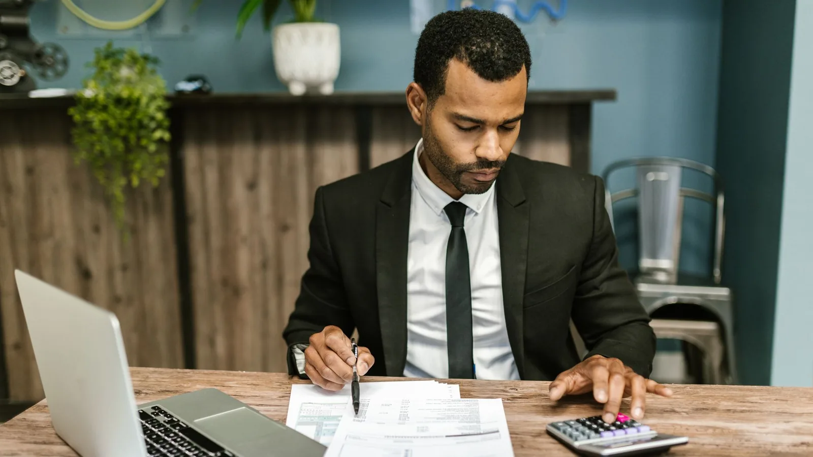 A man in a suit using a calculator alongside insurance paperwork, representing the valuation work involved in loss adjustment