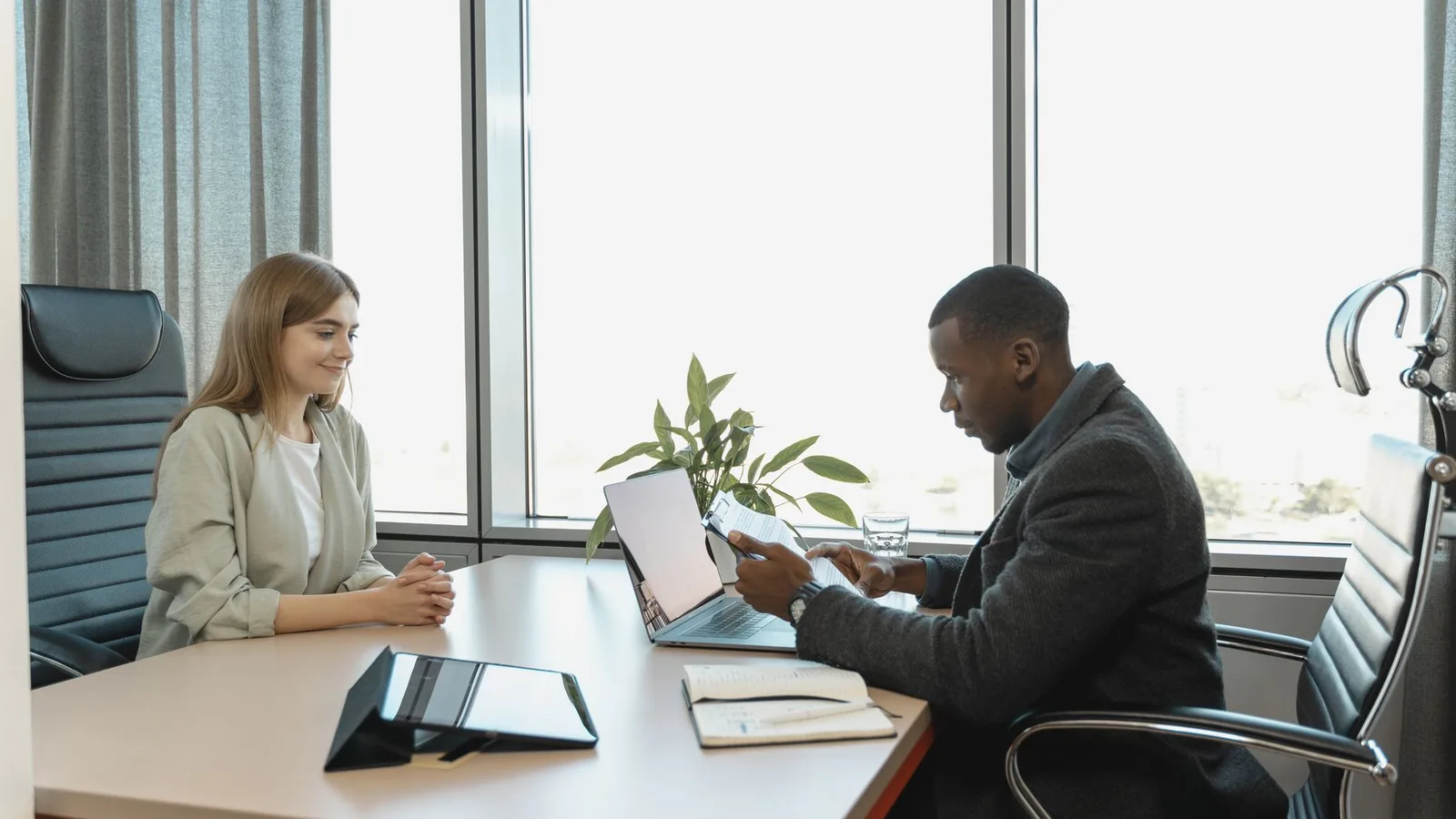 A man reviewing a candidate's paperwork across a desk during an interview, representing employee and pre-employment background checks