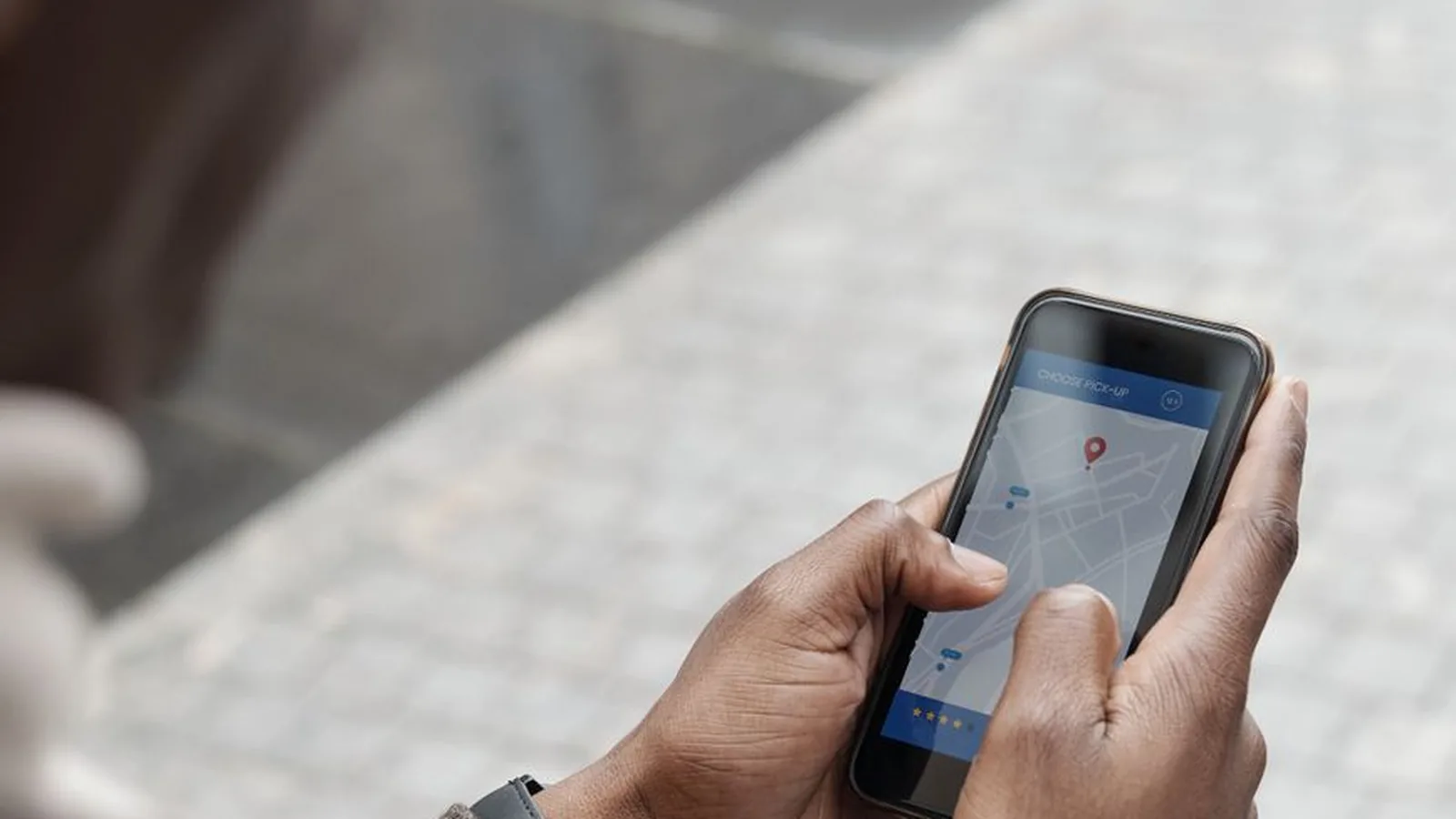 A hand holding a phone displaying a location pin on a map, representing asset and skip tracing work