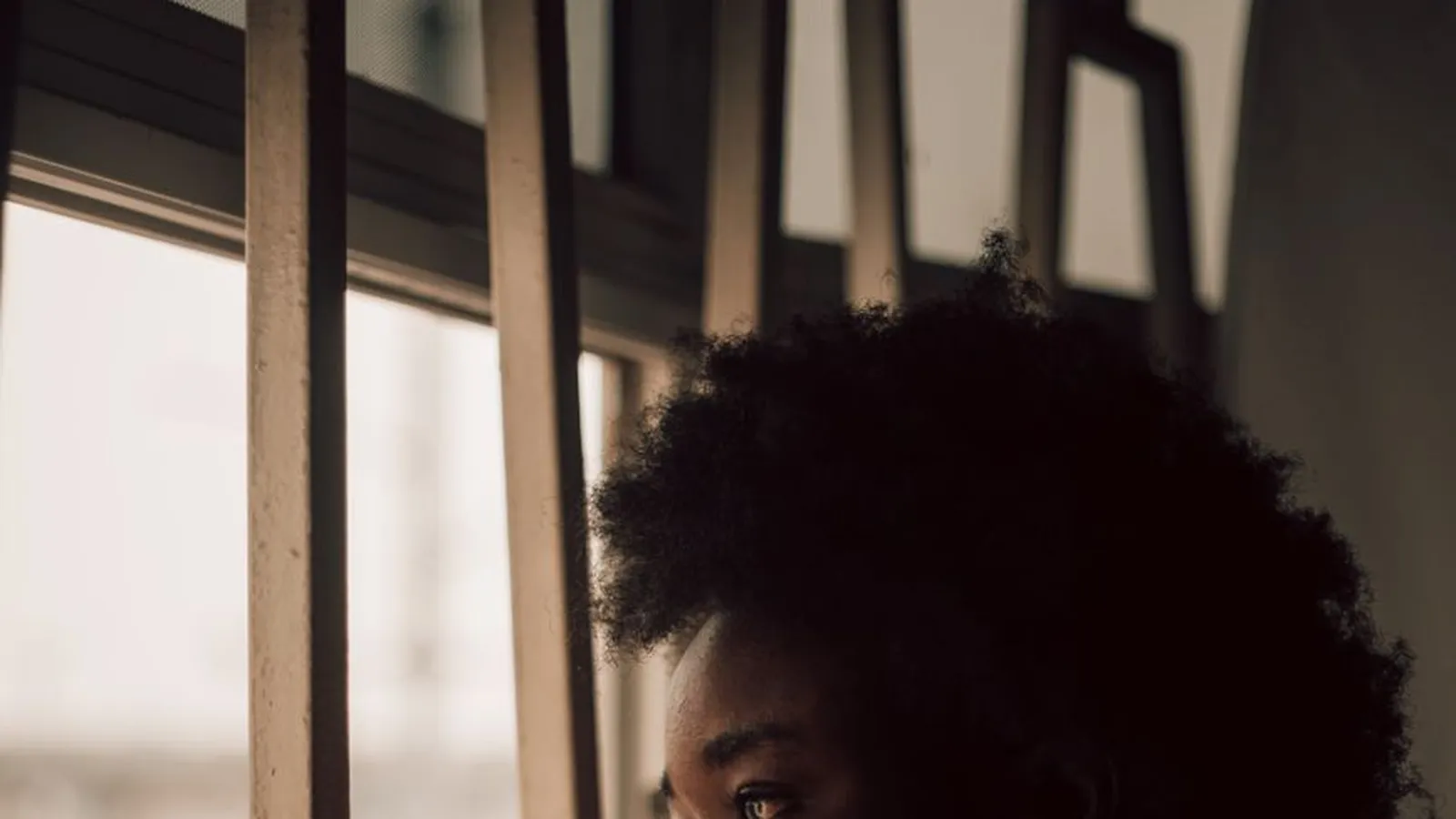 A woman sitting thoughtfully by a window, representing the uncertainty that eventually brings someone to hire a private investigator