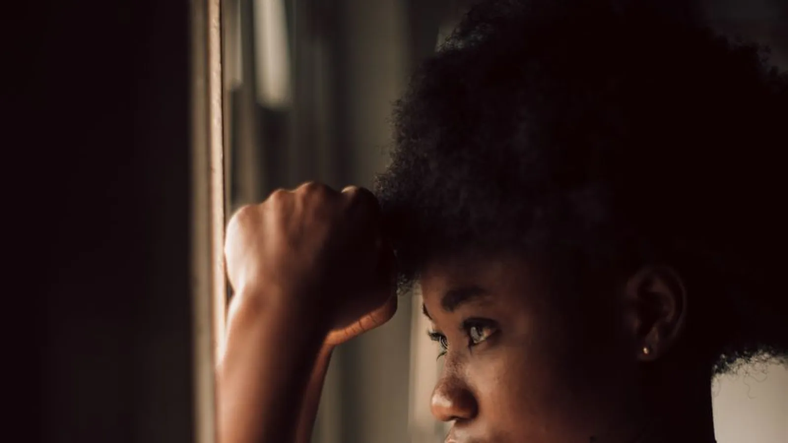 A woman standing by a window with her hand to her head, representing the weeks of uncertainty that usually precede a decision to investigate a relationship