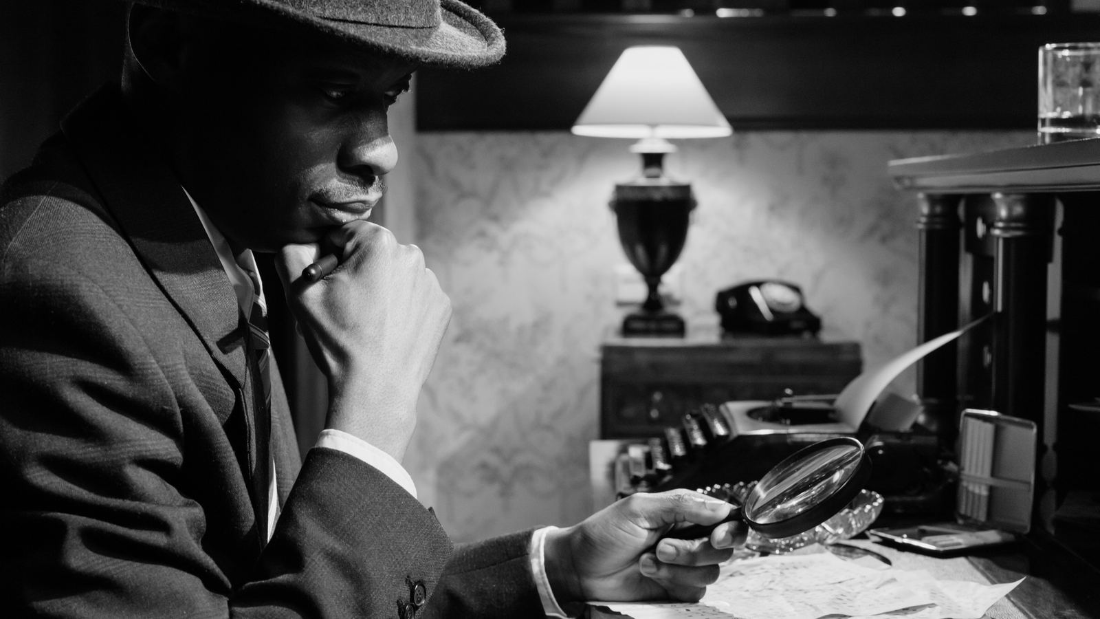 Private investigator examining case notes with a magnifying glass at a desk, representing the discreet, evidence-led work behind a matrimonial or partner investigation