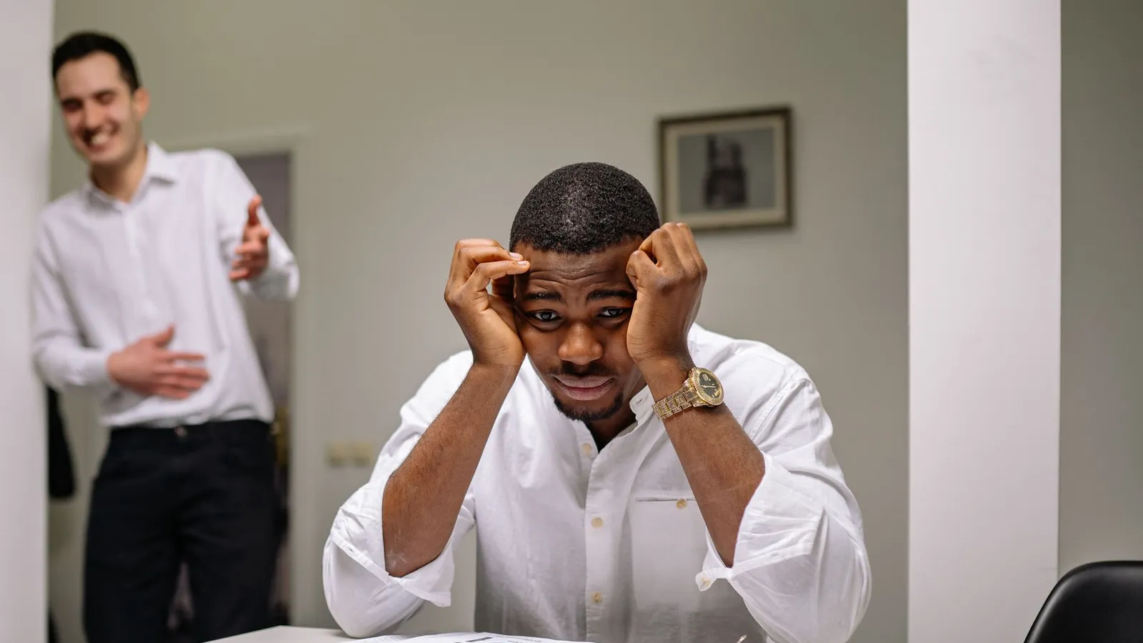 An employee sitting at his desk holding his head under pressure, representing a defensive reaction to routine questions about his area of work