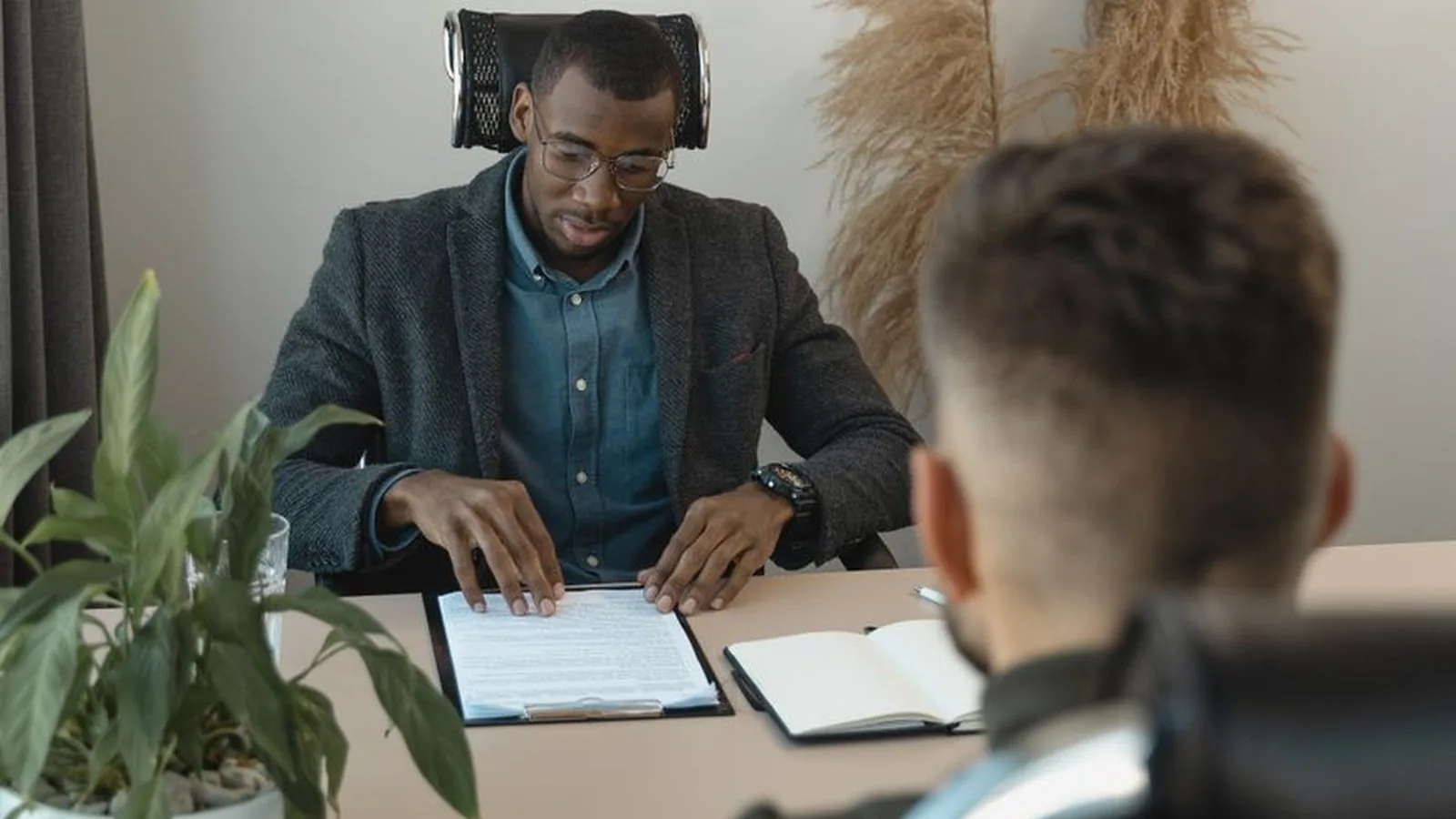 A man reviewing a candidate's paperwork across a desk during an interview, representing the moment a senior hire's story stops adding up