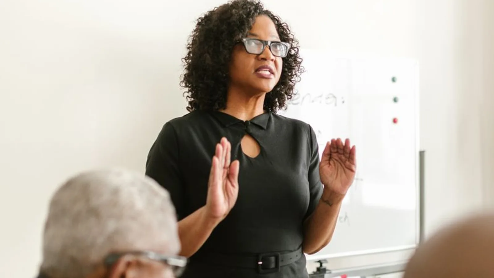 A woman leading a discussion in front of a whiteboard with colleagues seated around her, representing the oversight a registered firm structure provides